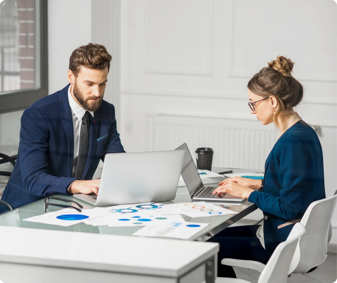 Two professionals working on laptops together.