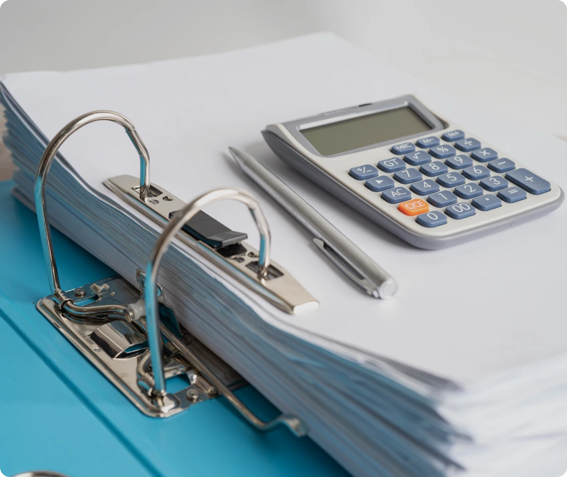 Binder, calculator, and pen on stacked papers.