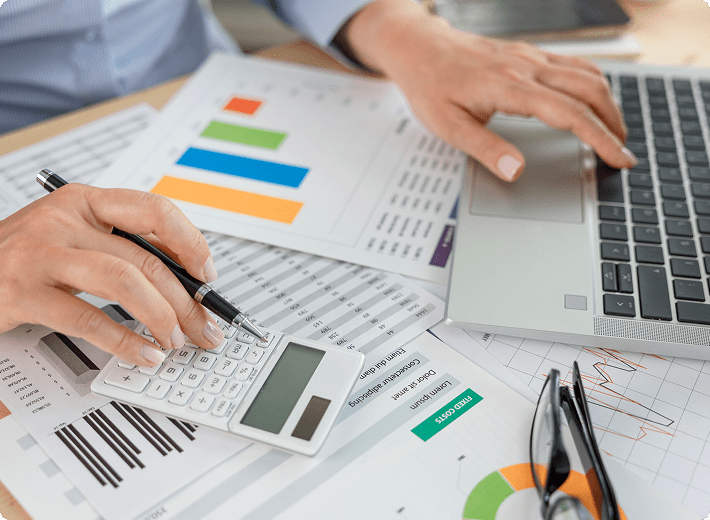 Person using calculator and laptop on graphs.