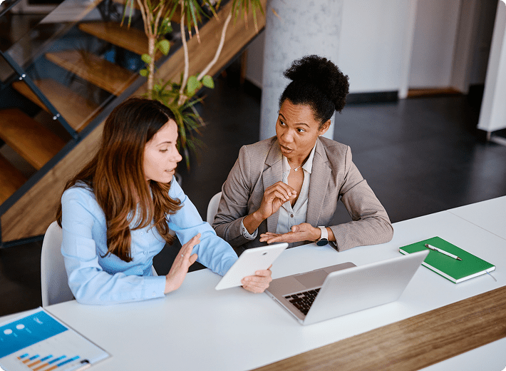 Two women discussing work at table.