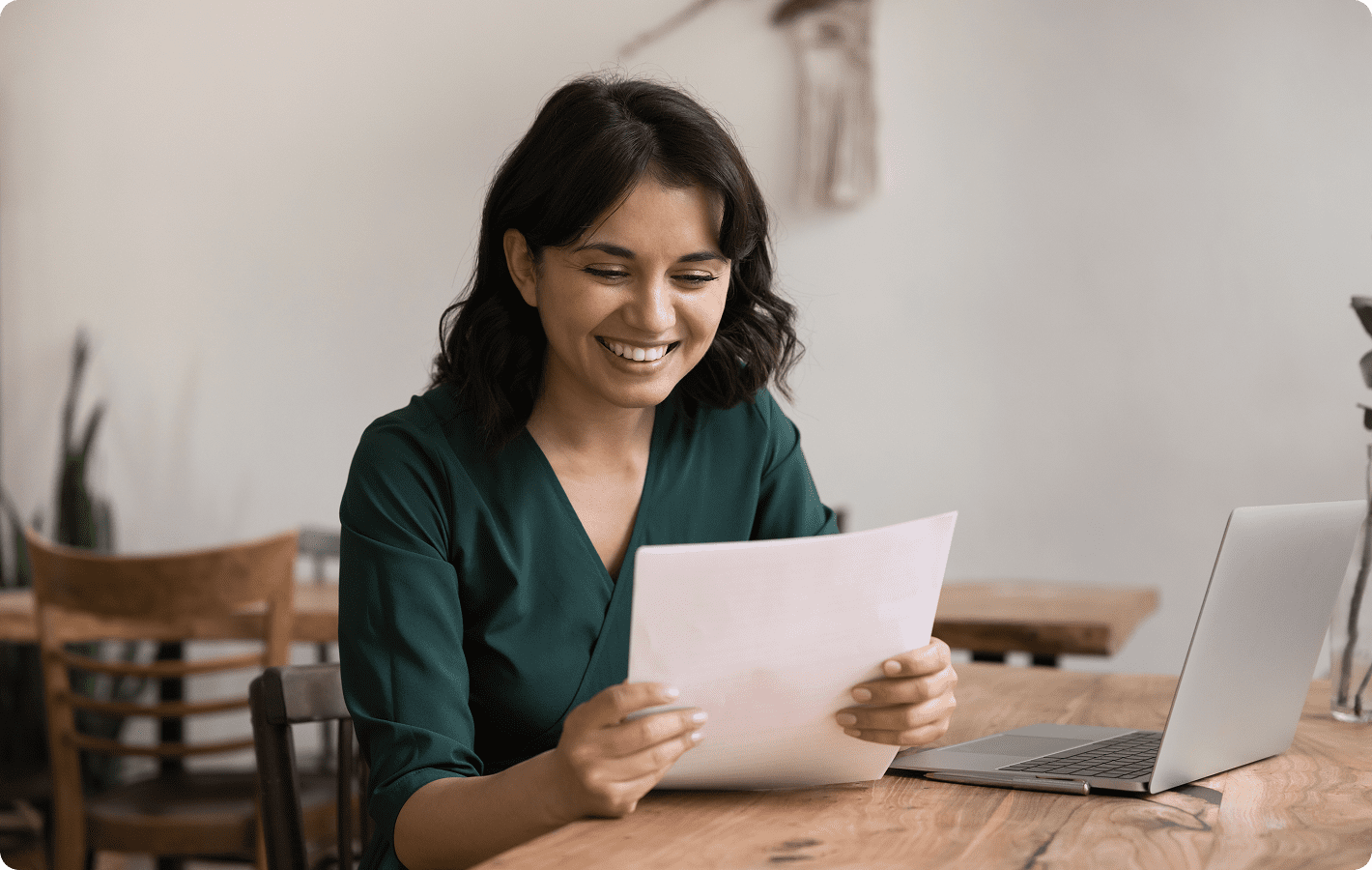 Woman reading document at wooden table, smiling.